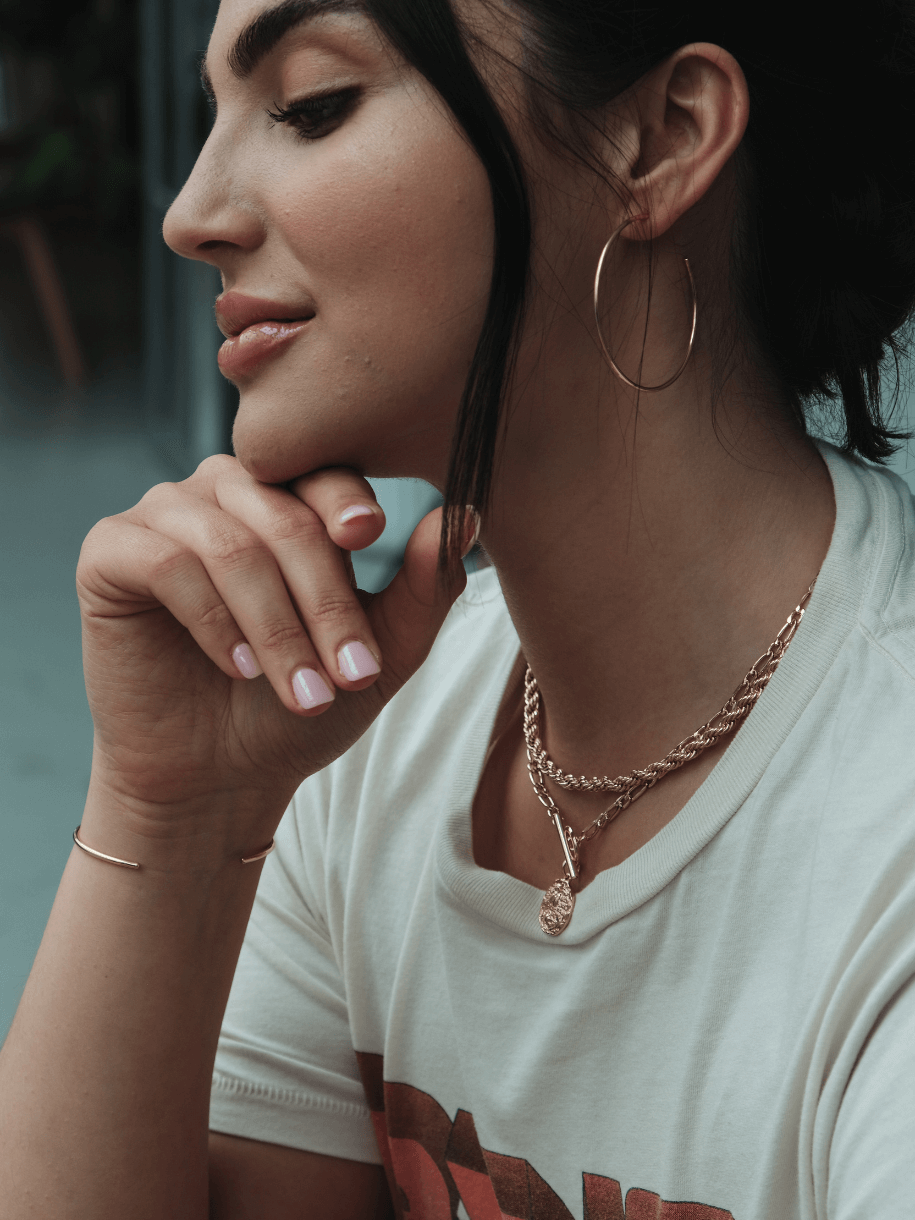 Woman in profile with Athena Toggle Coin gold jewelry and a white t-shirt.