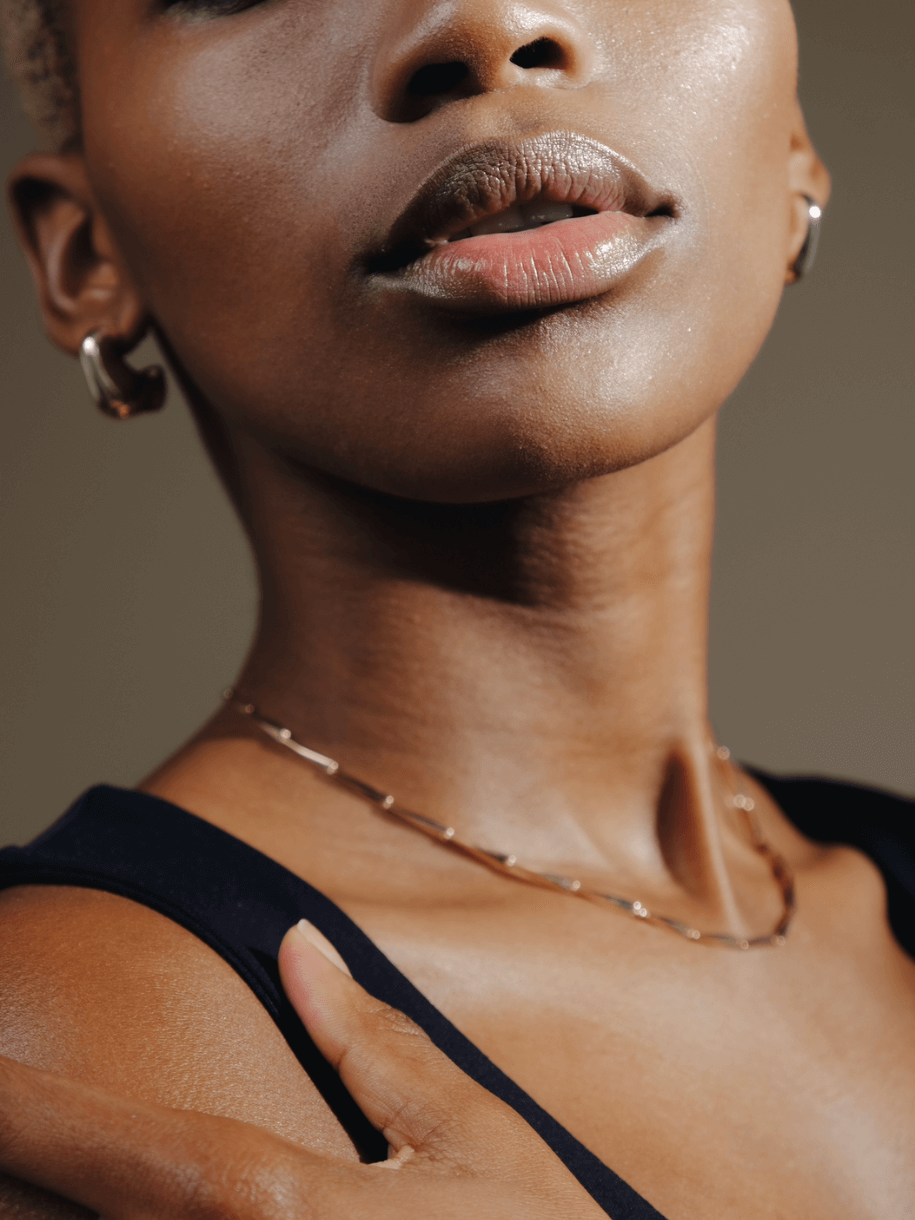 Close-up of a person with dark skin wearing a Parisian Layering Chain 14 inches and silver hoop earrings.