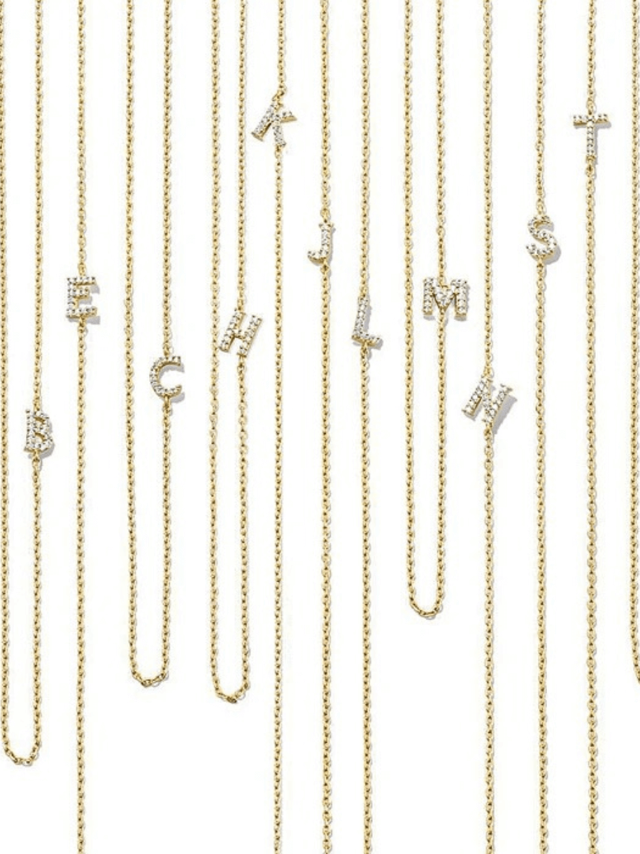 Multiple gold delicate necklace chains with letter pendants hang vertically.