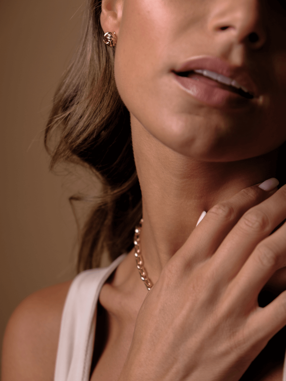 A woman with tan skin is wearing Knot Studs - Petite and a gold necklace.