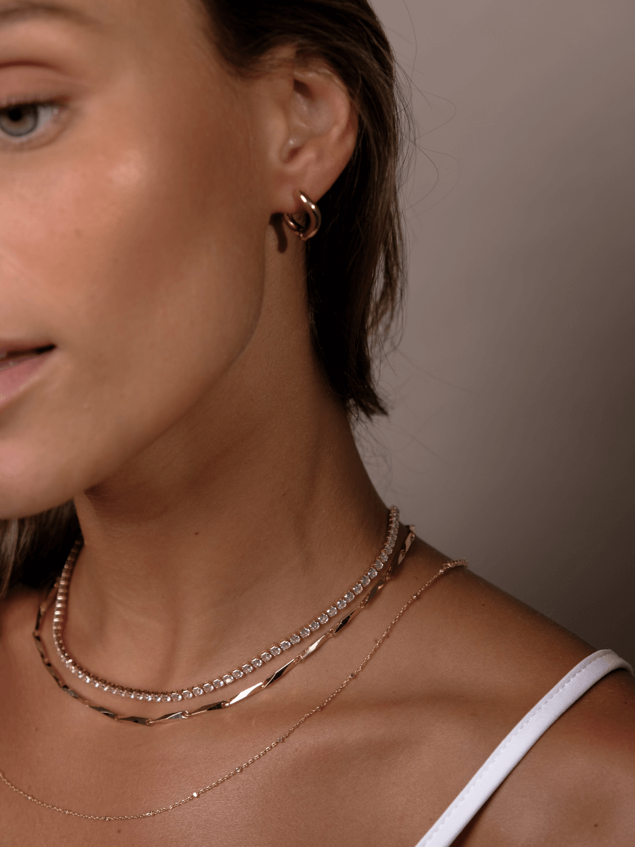 Close-up of a woman wearing hoop earrings and Parisian Layering Chain 14 inches necklaces.