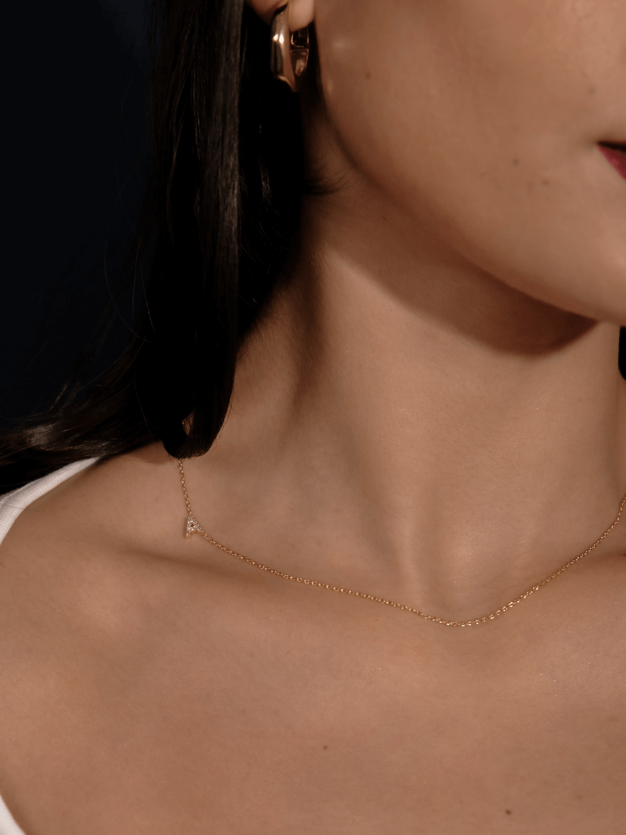 Close-up of a person's neck and shoulder wearing The Diamante Initials gold jewelry.