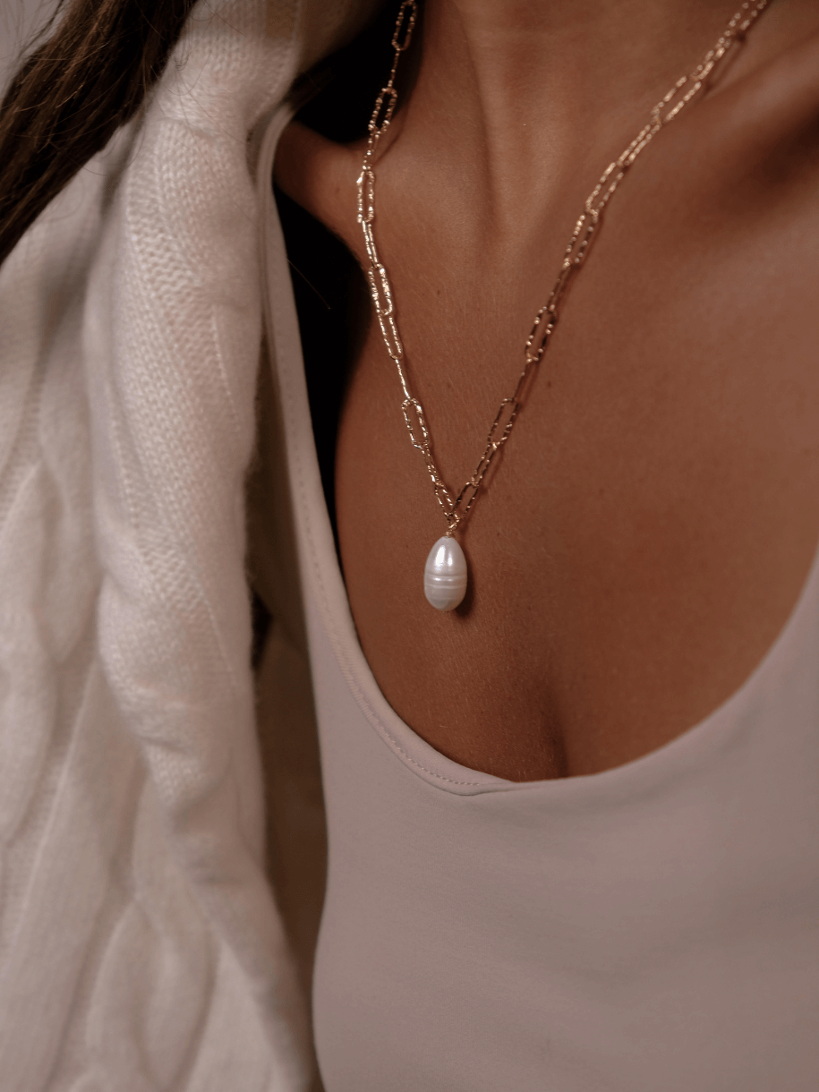 A woman wearing a gold chain necklace with a pearl pendant.
