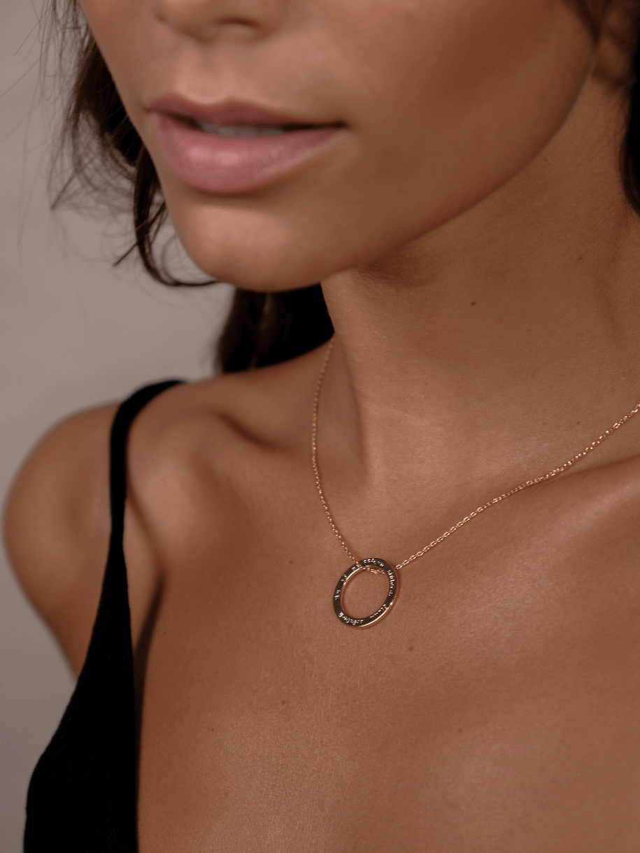 A woman wears an An té a bhíonn siúlach, bíonn scéalach - ROUND DISC gold necklace with a circular pendant.