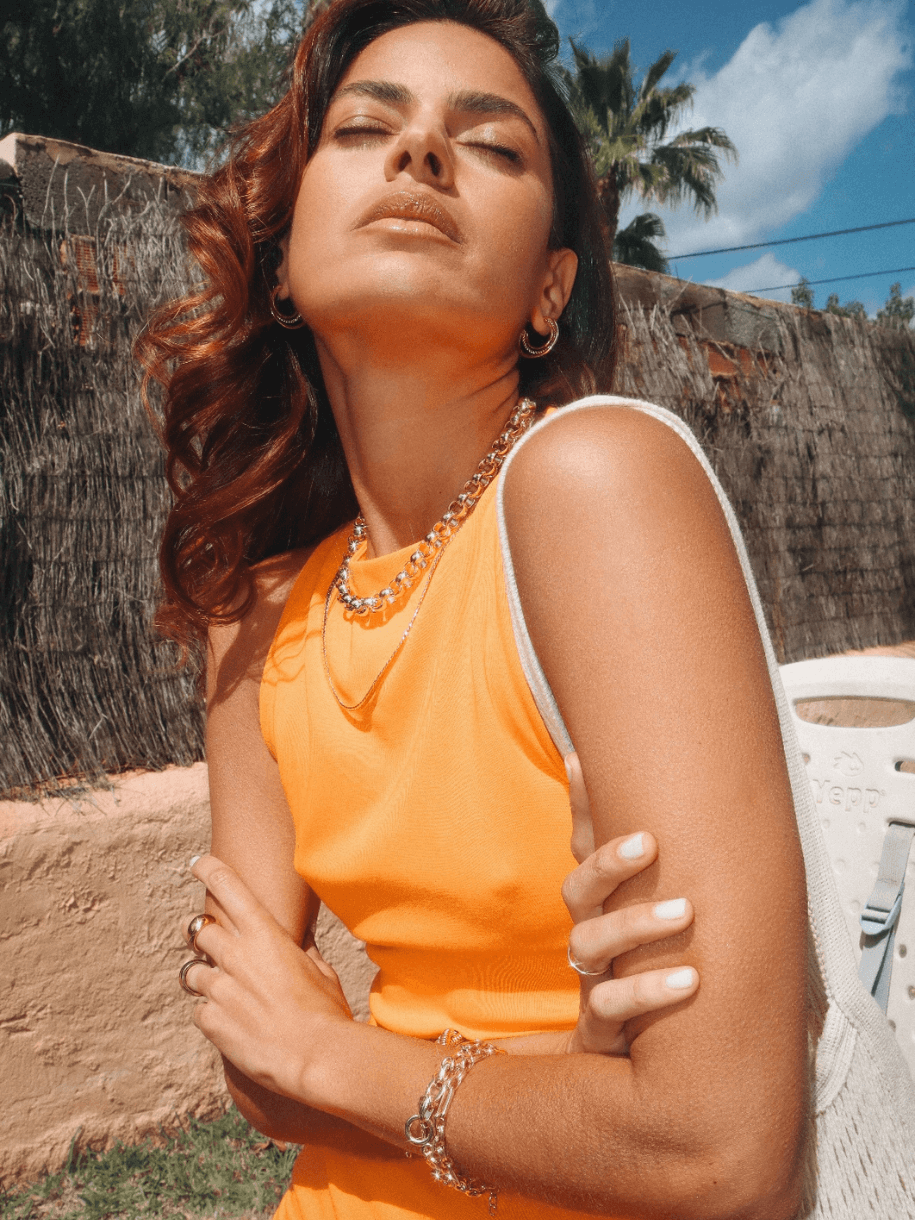 Woman in orange tank top and jewelry faces the sun with her eyes closed, wearing a Rolo Necklace.