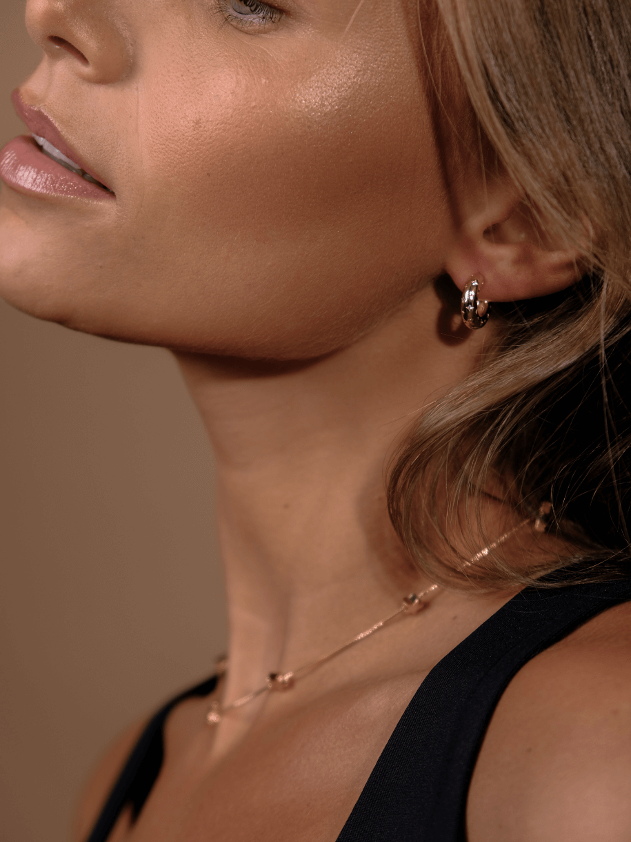 Close-up of a woman's face and neck, wearing Seeing Stars Hoop earrings and a delicate necklace.