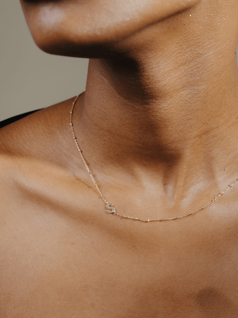 A woman wears a delicate gold Side Initial Letter Necklace with an "S" pendant.