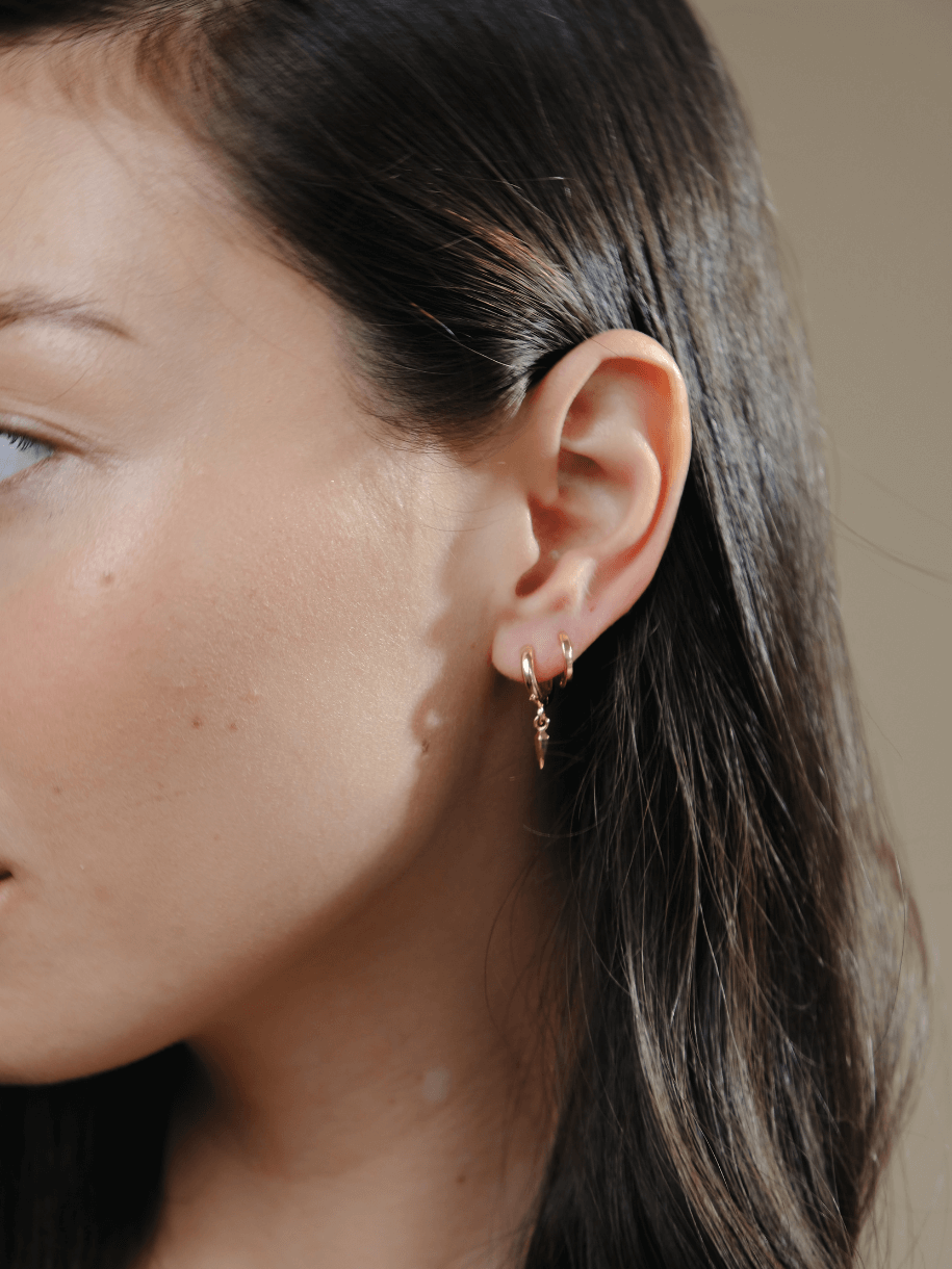Close-up of a woman's ear with two Huggie Hoop Gold earrings, one with a dangling charm.
