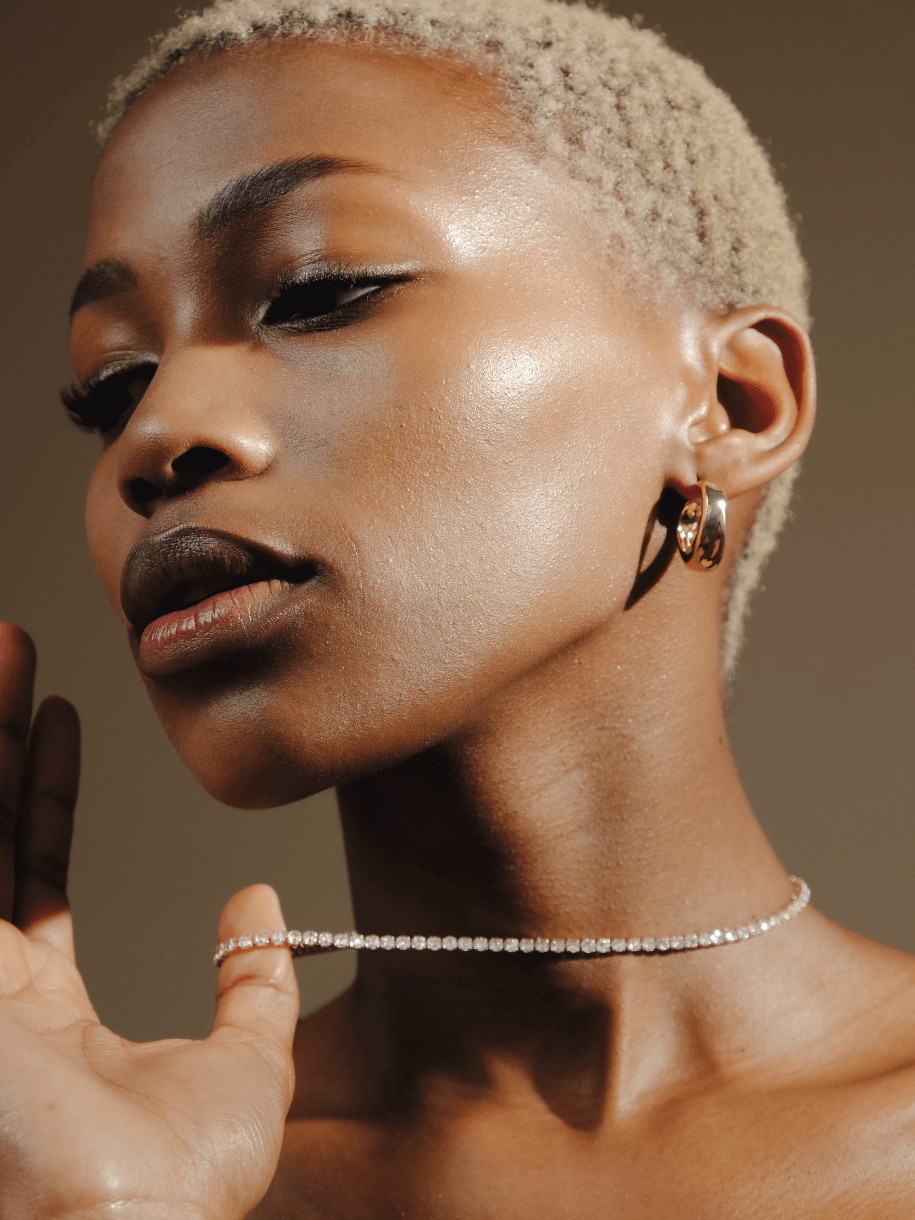 Close-up of a woman with short blonde hair wearing a diamond Tennis Necklace - Clear Gemstone and gold hoop earrings.