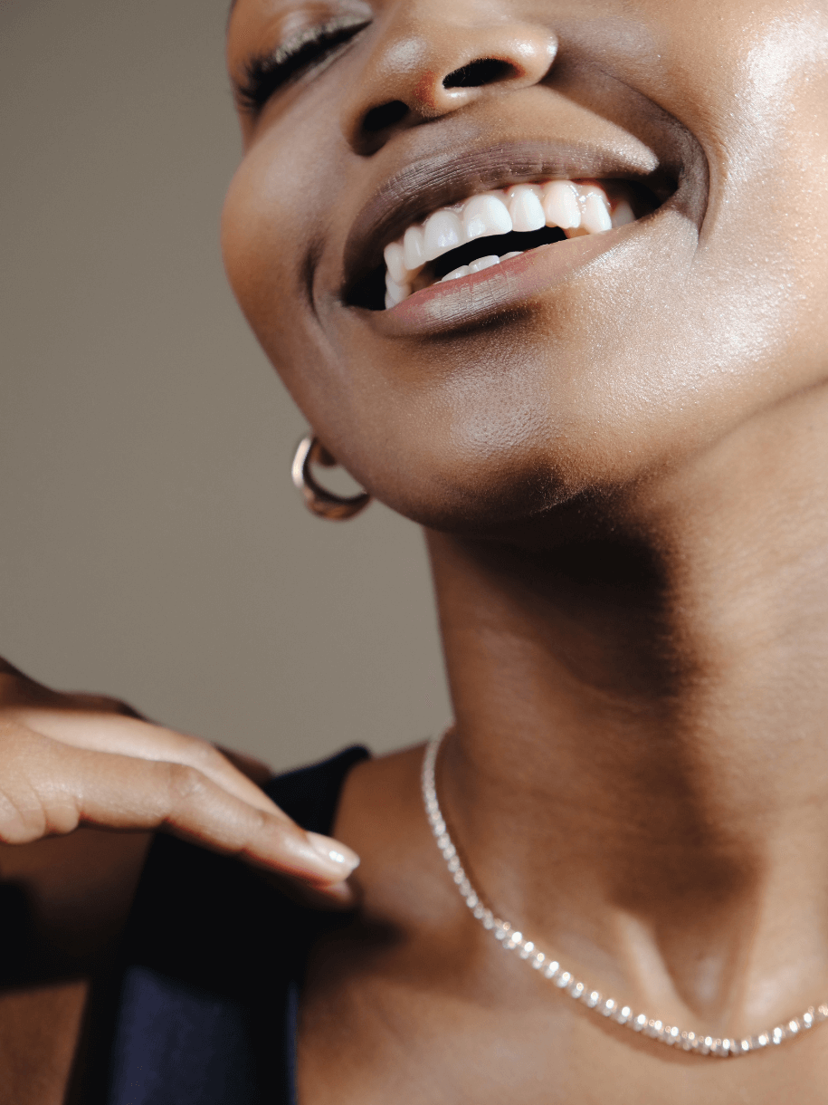 Close-up of a smiling woman with dark skin, wearing Tennis Necklace - Clear Gemstone.