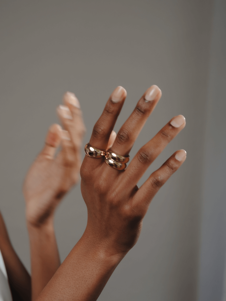 Two dark-skinned hands, one with a gold Double Dome Ring, reach toward the viewer.