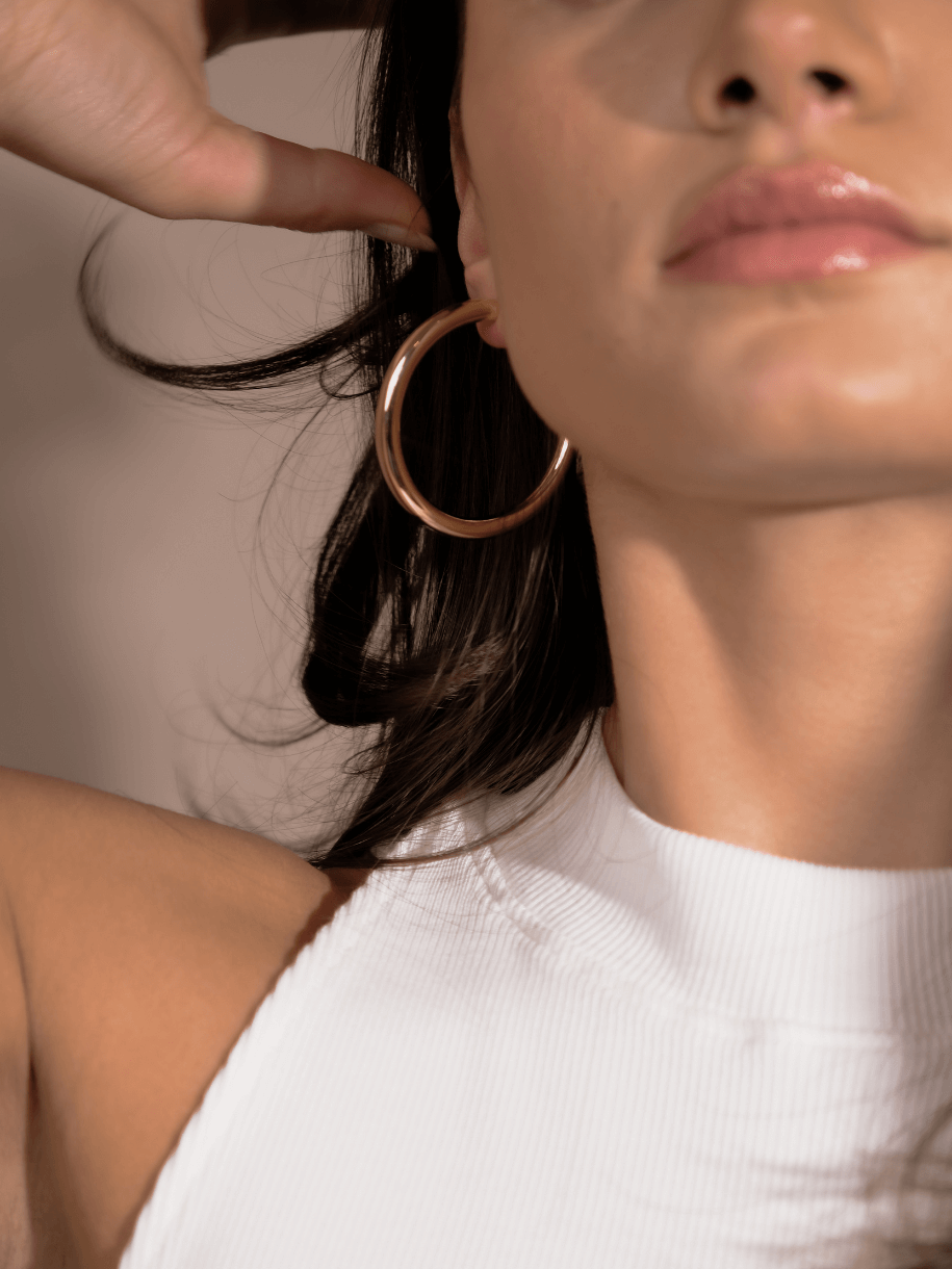 Close-up of a woman's face and shoulder, wearing Alexa Gold Hoops and a white top.