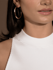 Close-up of a woman wearing Alexa Gold Hoops and a white ribbed top.