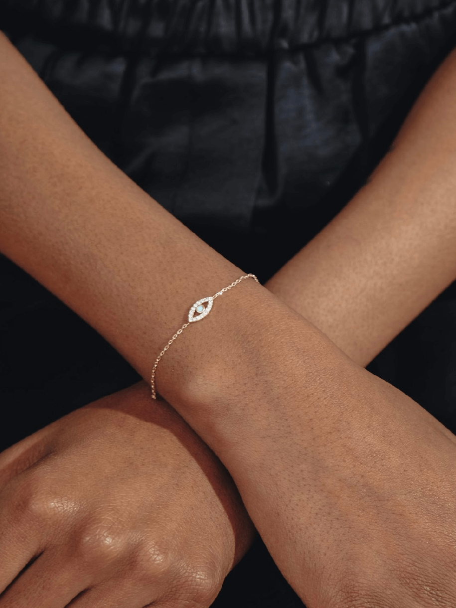 A crossed pair of arms wearing an Evil Eye - Turquoise bracelet with an eye-shaped charm.