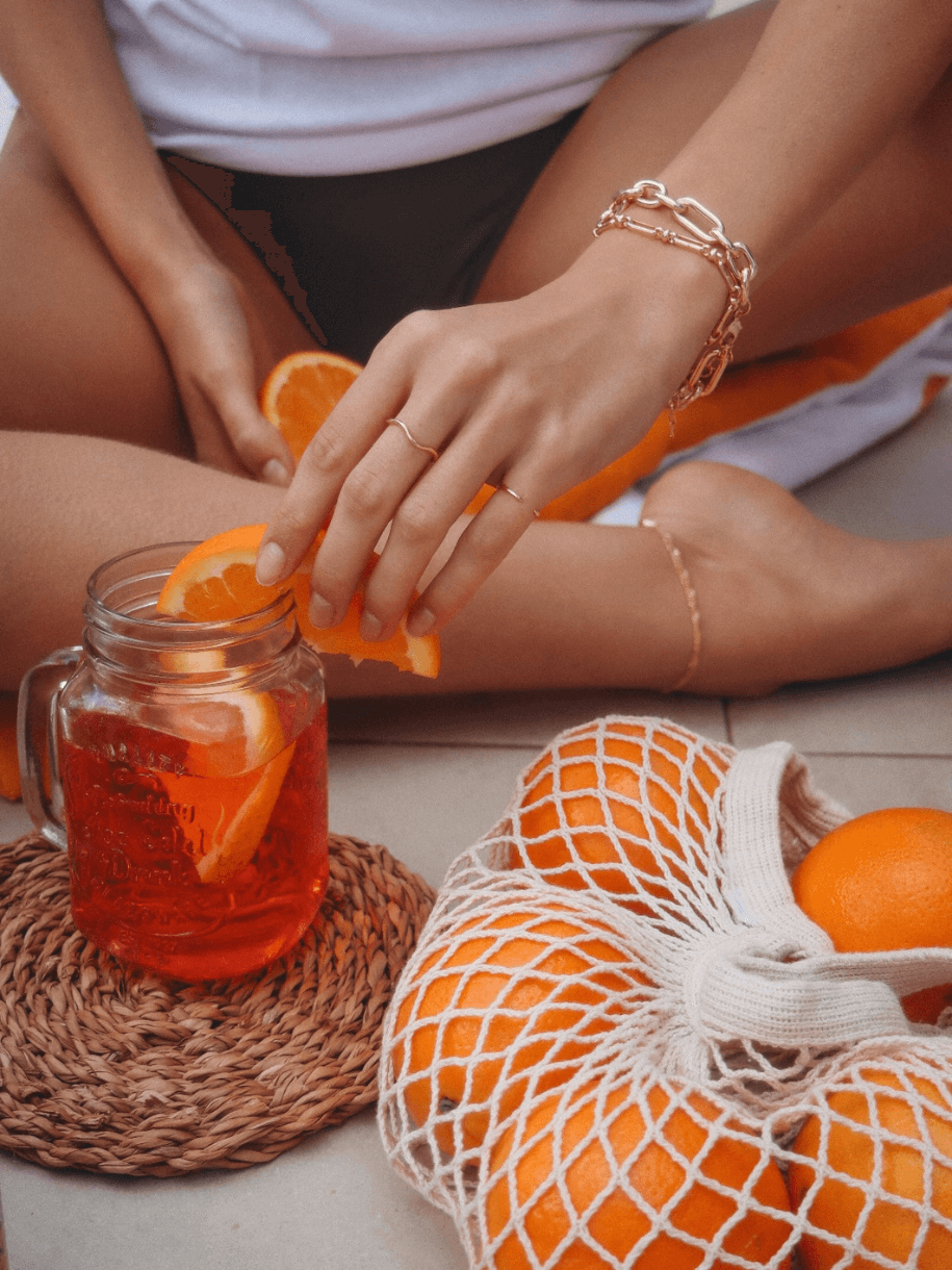 A person adds an orange slice to a drink, with a bag of Wave Ring oranges nearby.
