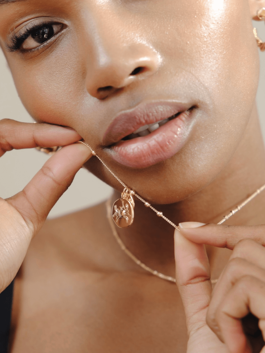 Close-up of a woman with shiny skin holding a gold Leo Zodiac Coin necklace with a zodiac pendant.