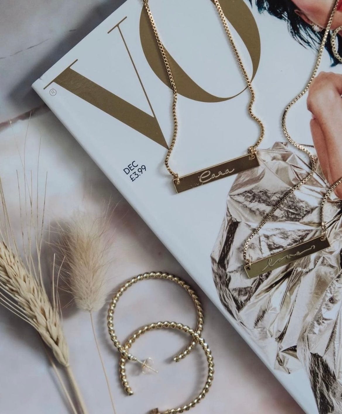 Gold Cara Bar Necklace and hoop earrings arranged on a magazine with wheat stalks.