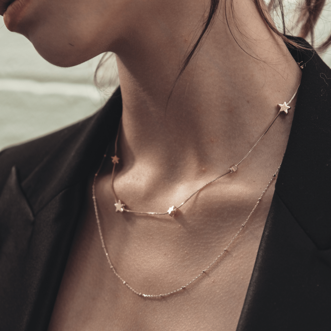 Close-up of a person wearing The Box Multi Star two-strand necklace, one with star charms, under a black blazer.