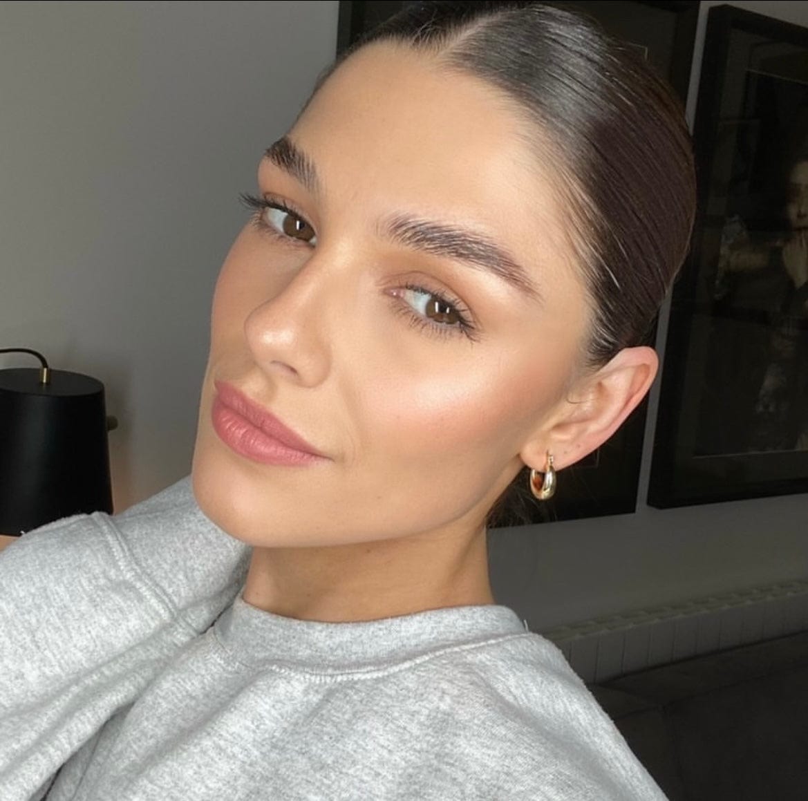Close-up of a woman with slicked-back hair, wearing a grey sweatshirt and gold Chunky Huggie Hoop earrings.