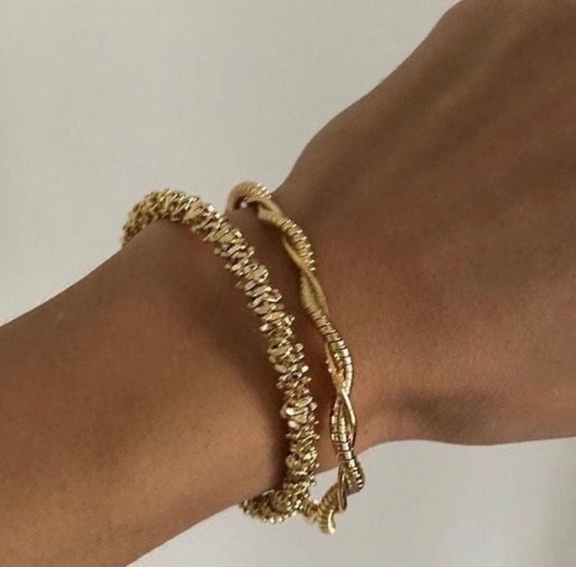 A person's wrist wearing two gold-toned Jagged Bracelets.