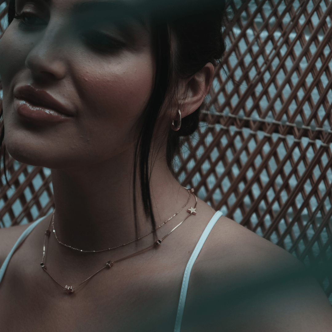 A woman with dark hair wears Mini Square Gold Hoop earrings, against a woven background.