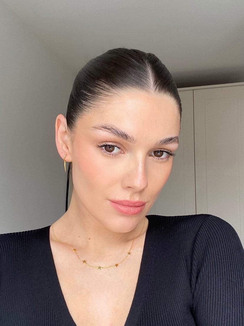 A woman with slicked-back dark hair, wearing a Celebrate: Wish Upon A Star gold star necklace and gold earrings.