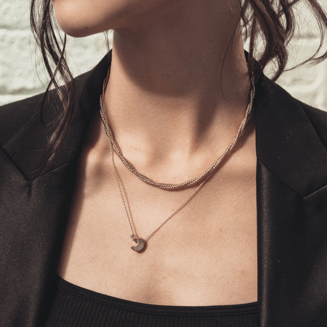 Close-up of a woman's neck wearing two necklaces, one with a Stacked Moon and Star pendant, and a black blazer.