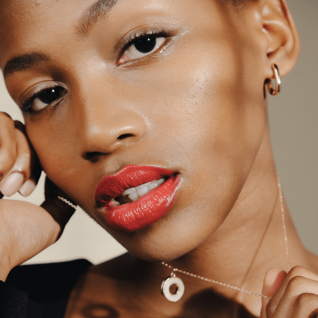 Close-up of a woman wearing Mini Square Gold Hoop earrings, red lipstick, gold jewelry, and neutral background.