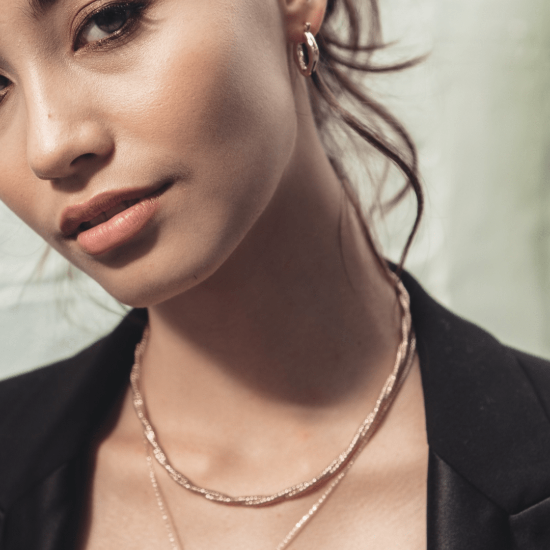 Close-up of a woman wearing gold Crossing Twisted Chain and a black blazer.