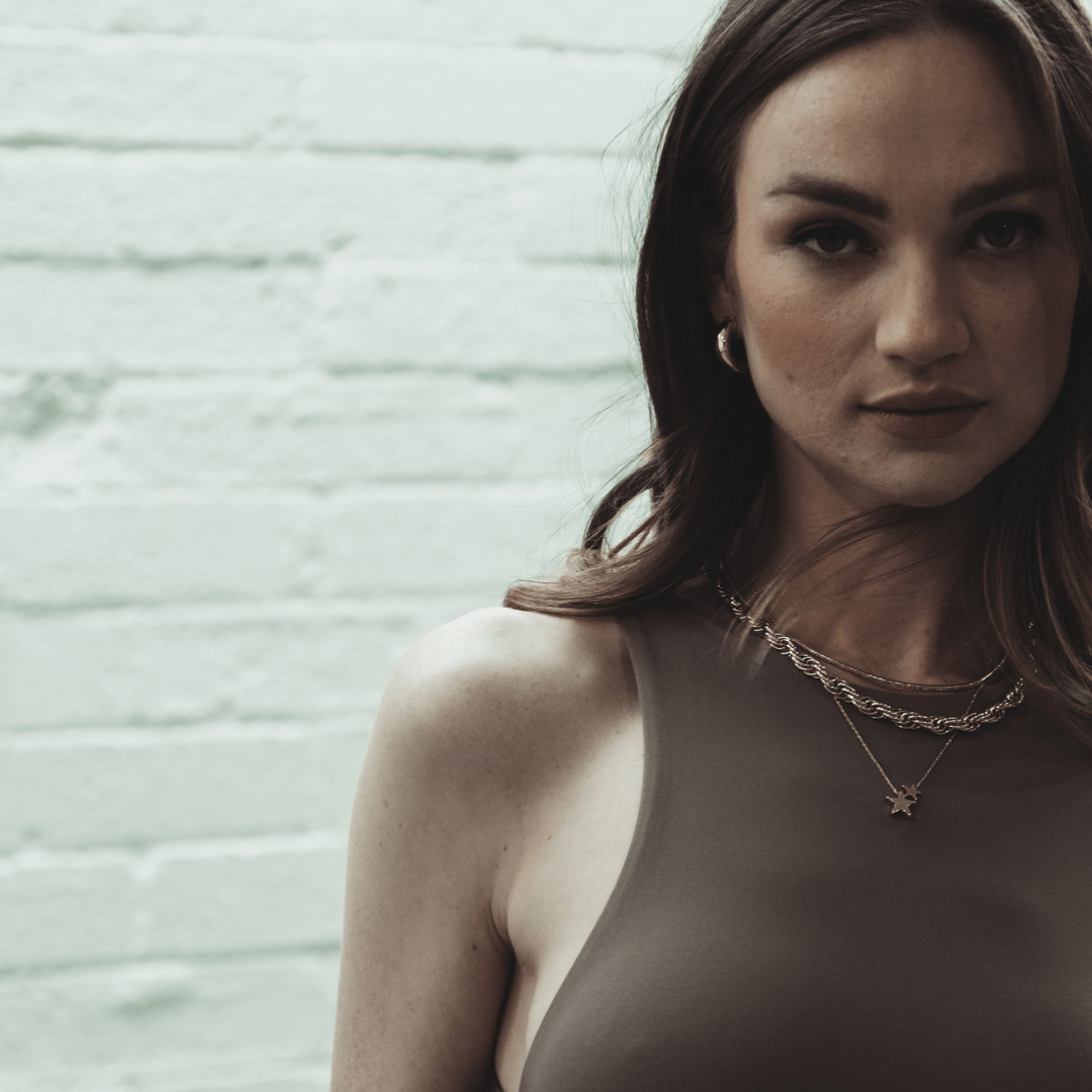 Portrait of a woman wearing Stacked Star jewelry against a light-colored brick wall.
