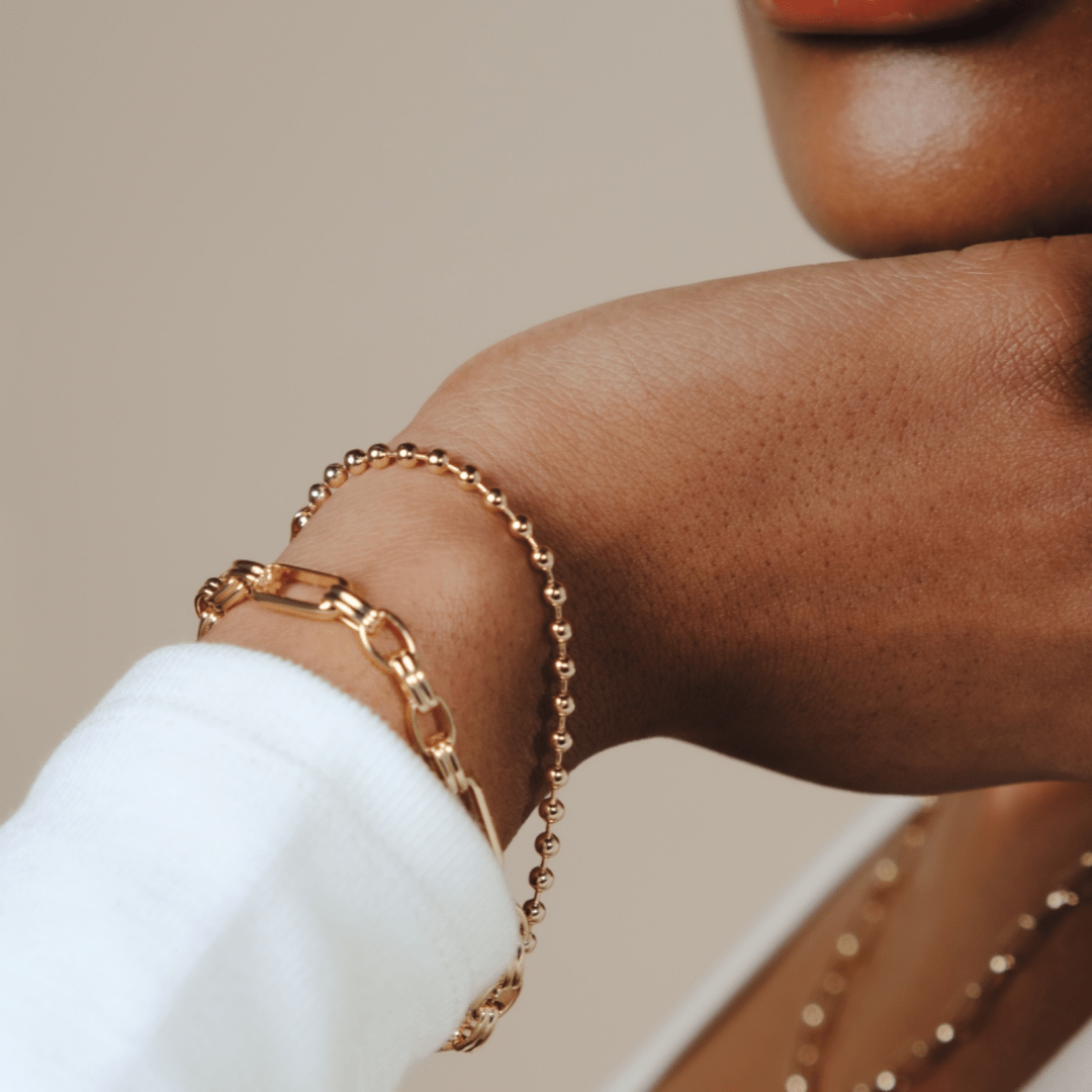 Close up of a person's wrist wearing two gold Triple Link Bracelets.