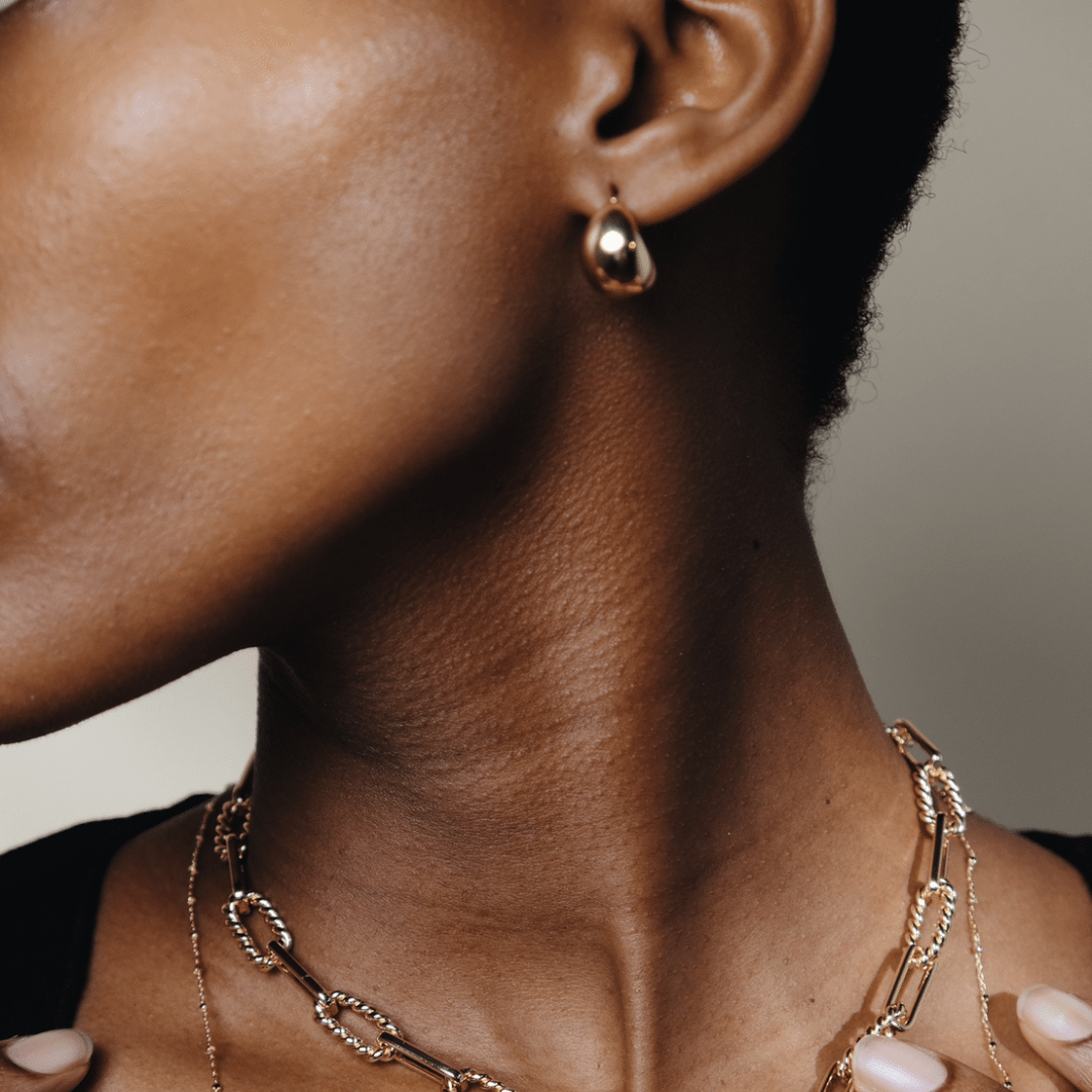 Close-up of a person with gold Dome Hoops and layered gold necklaces.