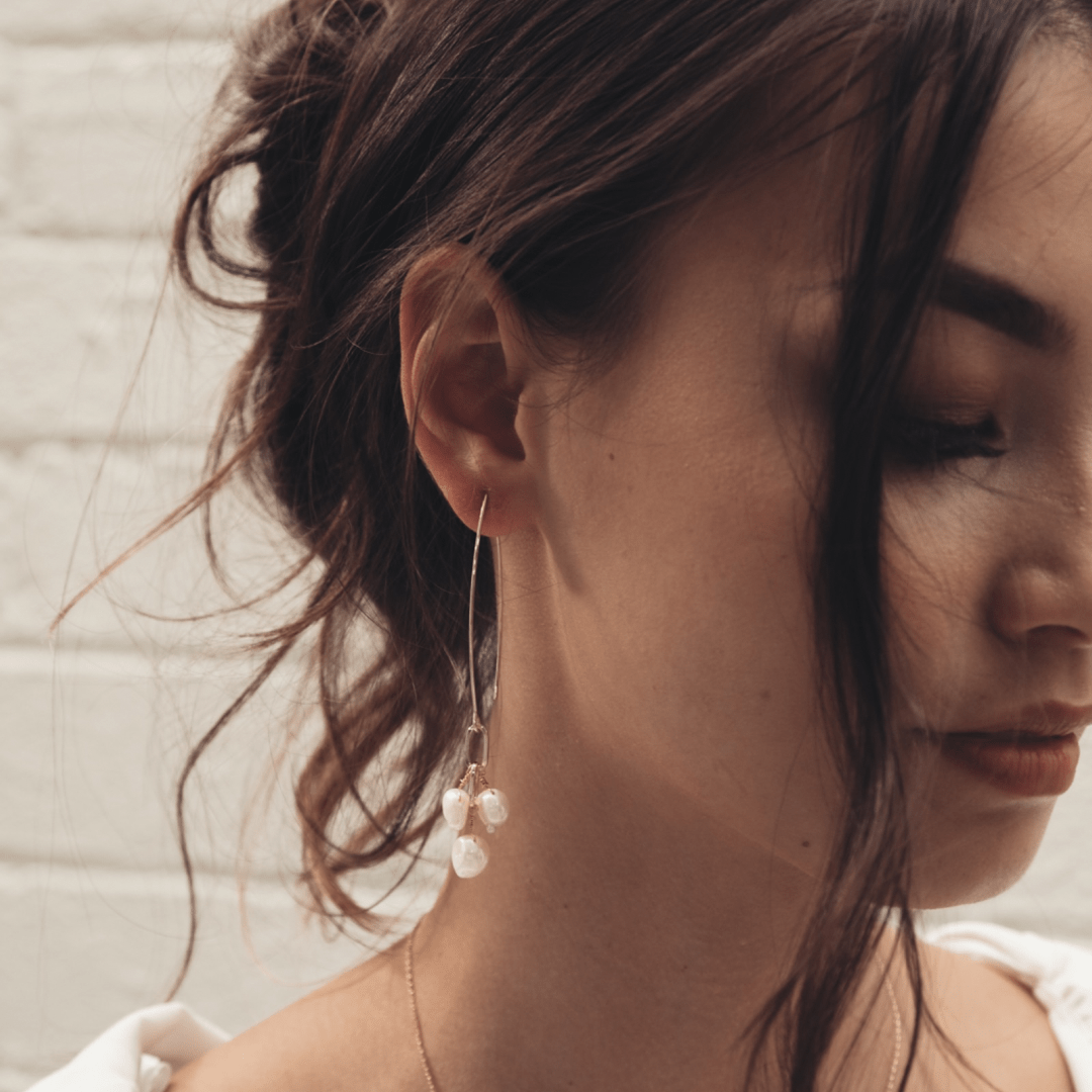 A person with dark hair and a Bridal Fishbone Pearl earring is looking down.