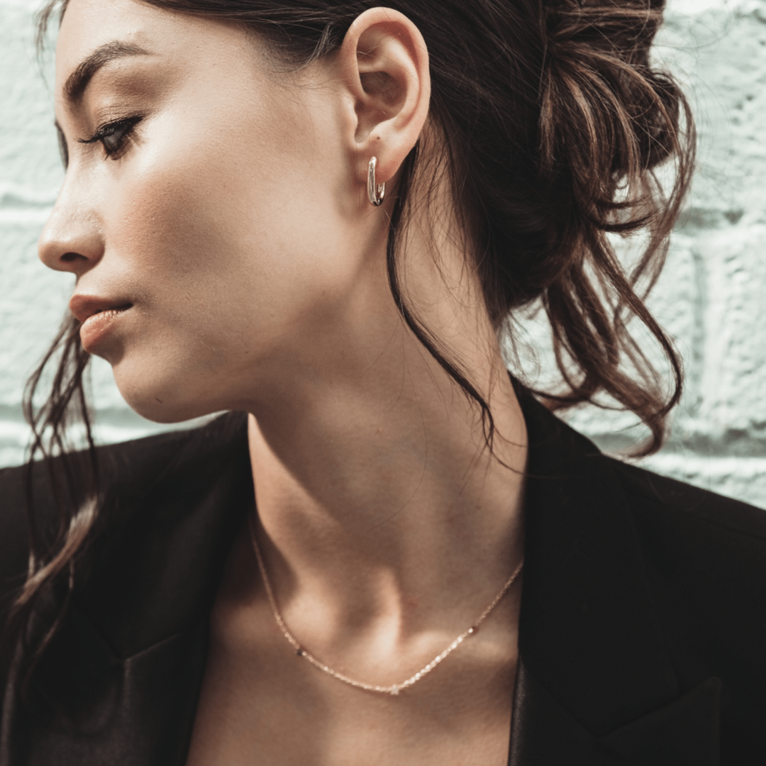 Profile of a woman wearing Mini Square Gold Hoop earrings and necklace, with a black jacket.