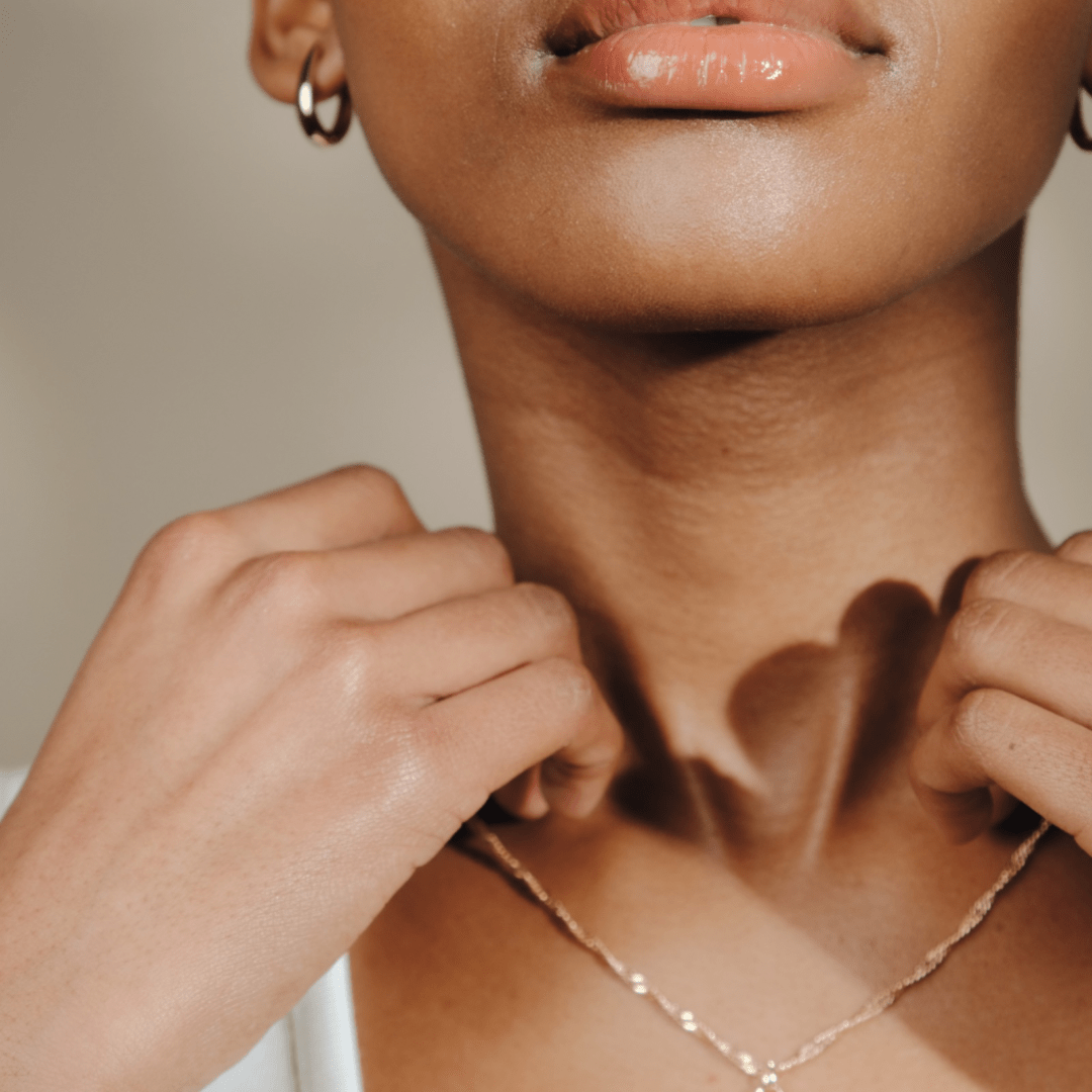 Close up of a person's neck and upper chest, adjusting a gold Claw Hoop.