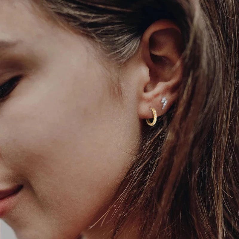 Close-up of a woman's ear with a Skinny Bar Diamanté Huggie Hoop and a lightning bolt stud.