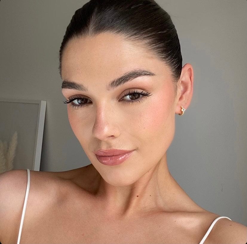 Close-up of a woman with dark hair styled back, wearing light makeup and a white tank top and Evil Eye Huggie Hoop earrings.