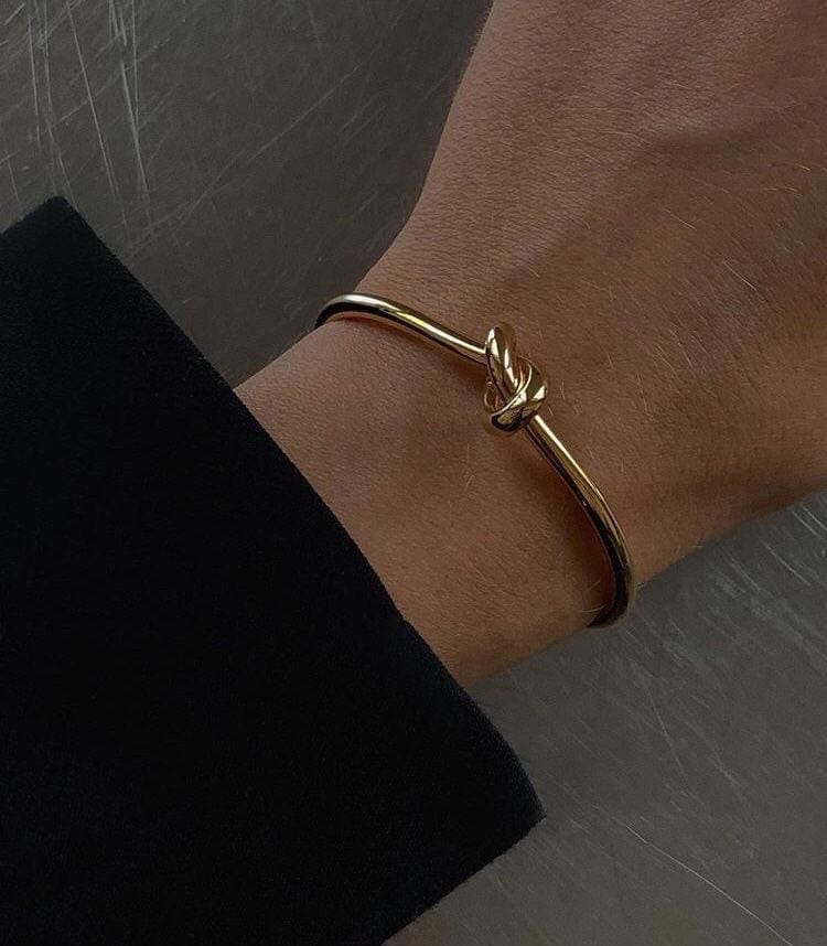 A gold Knot Bangle on a wrist.