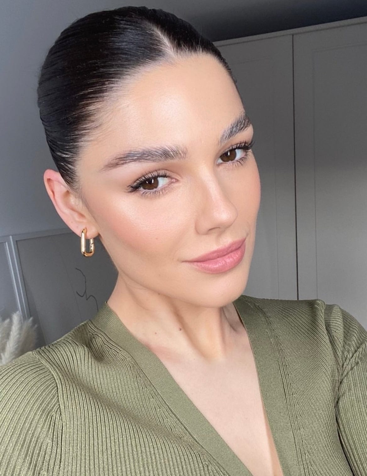 A woman with dark hair pulled back, wearing a green top and gold earrings, poses for a close-up shot, wearing Mini Square Gold Hoops.