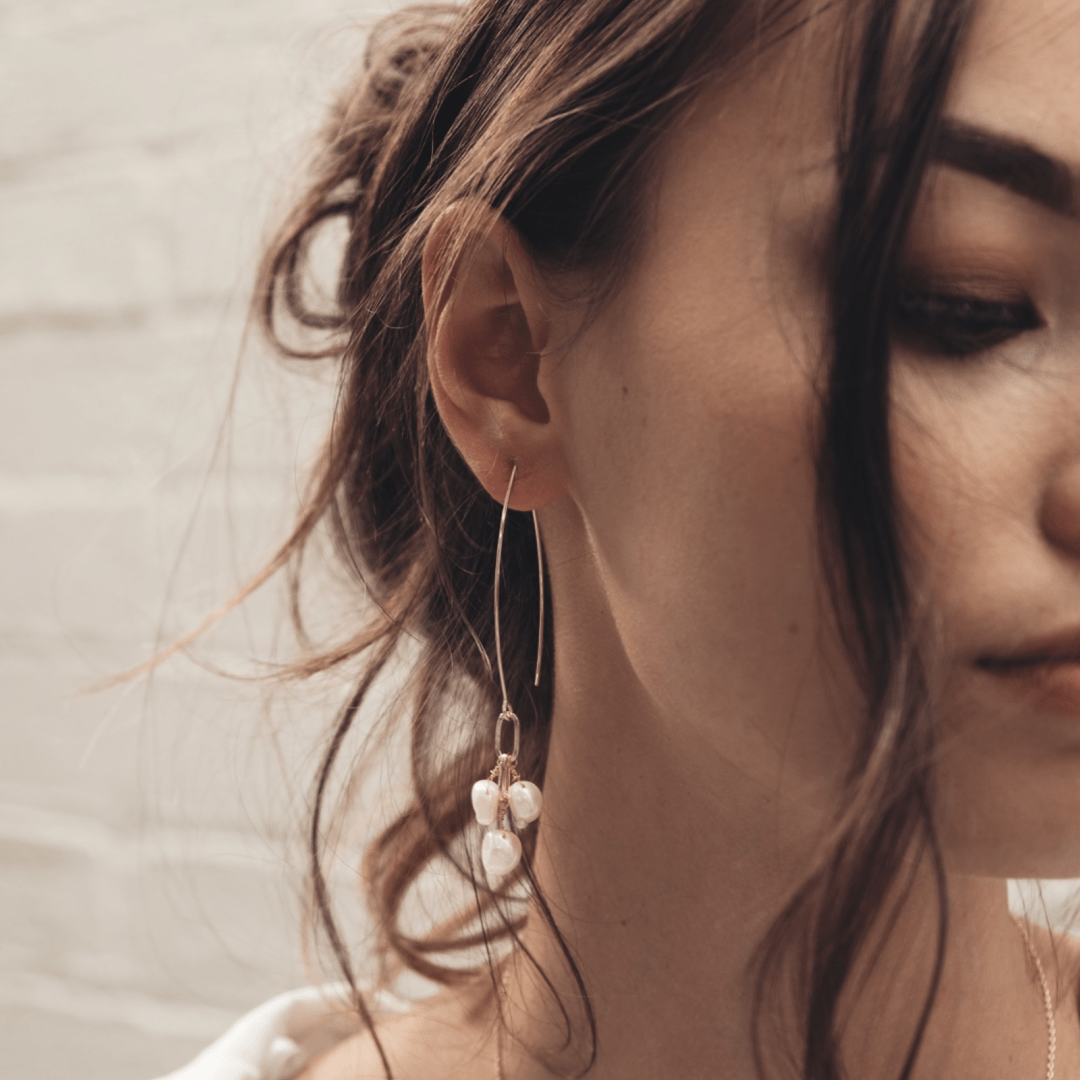 A woman with brown hair wears a Bridal Fishbone Pearl earring.
