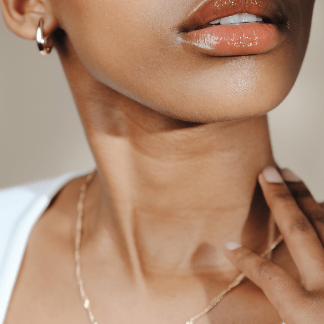 Close-up of a person's neck, lips with gloss, and gold Claw Hoop jewelry.