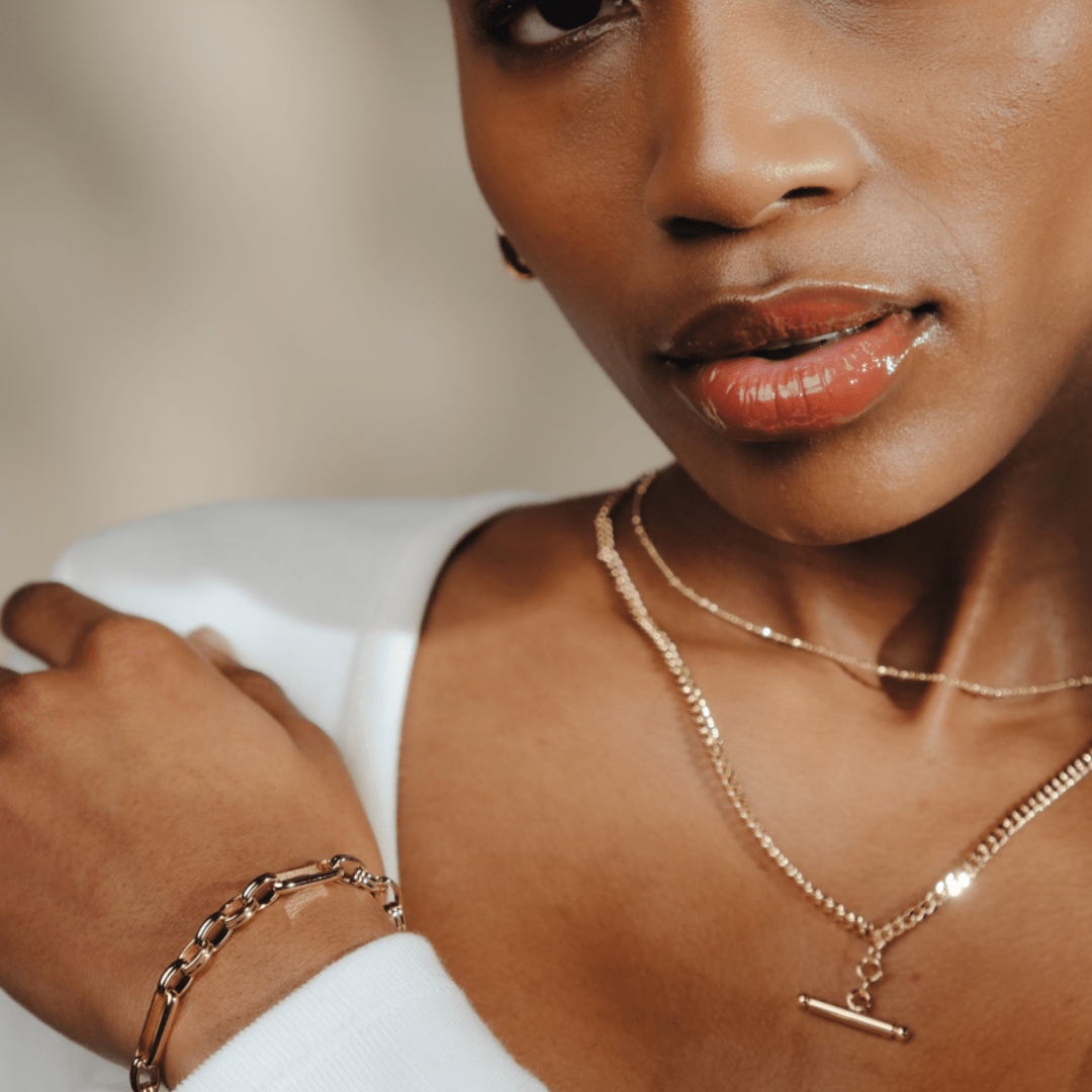 Close up of a woman wearing a T-Bar Curb Chain bracelet and layered gold necklaces.