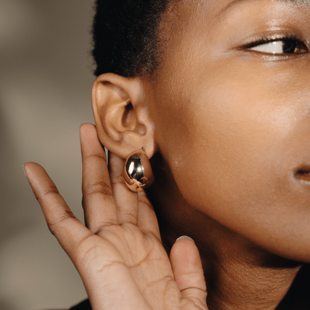 Close-up of a person with dark skin wearing a Twilight Moon Hoop earring and touching their ear.