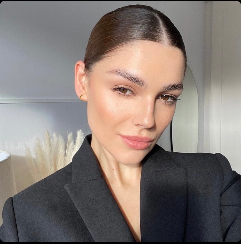 A woman with slicked-back brown hair wearing a black blazer looks at the camera, showcasing the Huggie Hoop Gold.