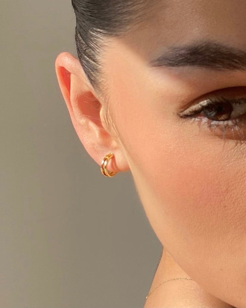 Close-up of a person's ear with a Double Bar Gold Huggie Hoop earring.