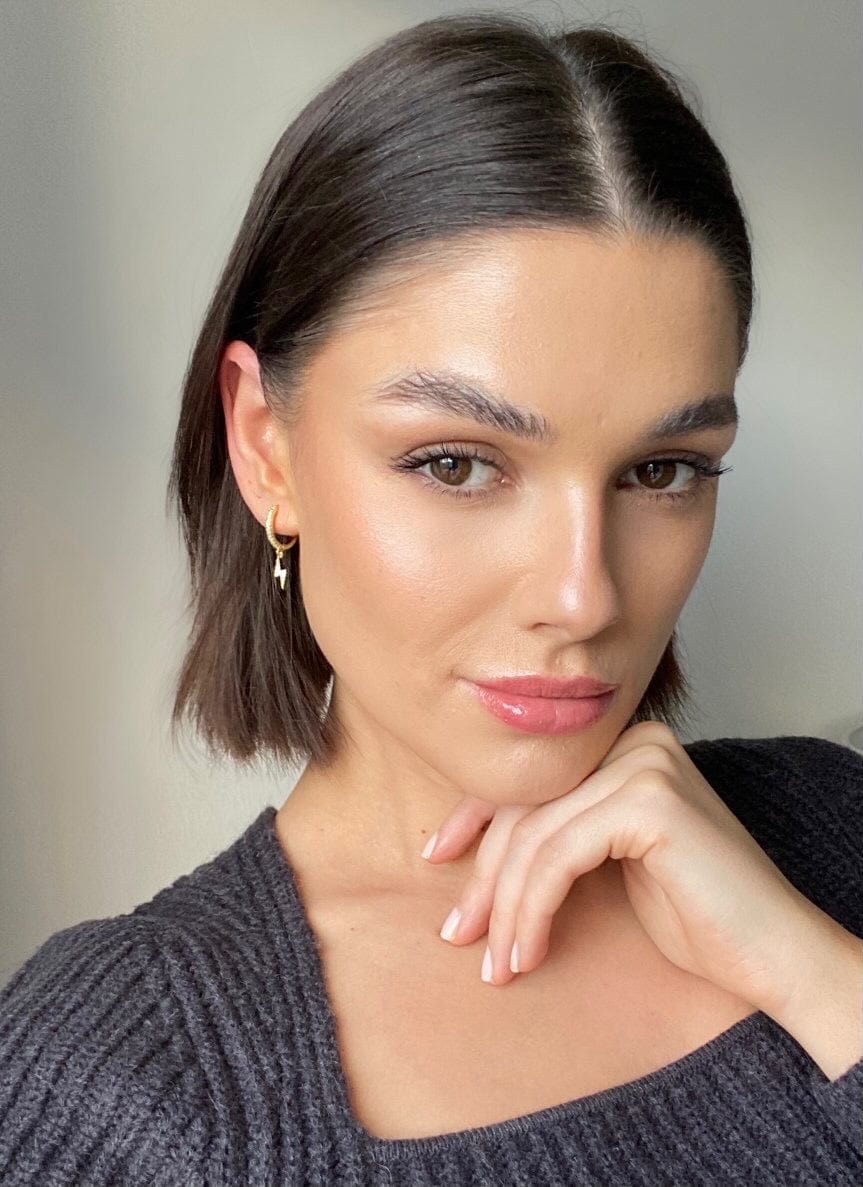 A portrait of a woman with brown hair and a gray sweater wearing Bolt Huggie Hoop Silver.