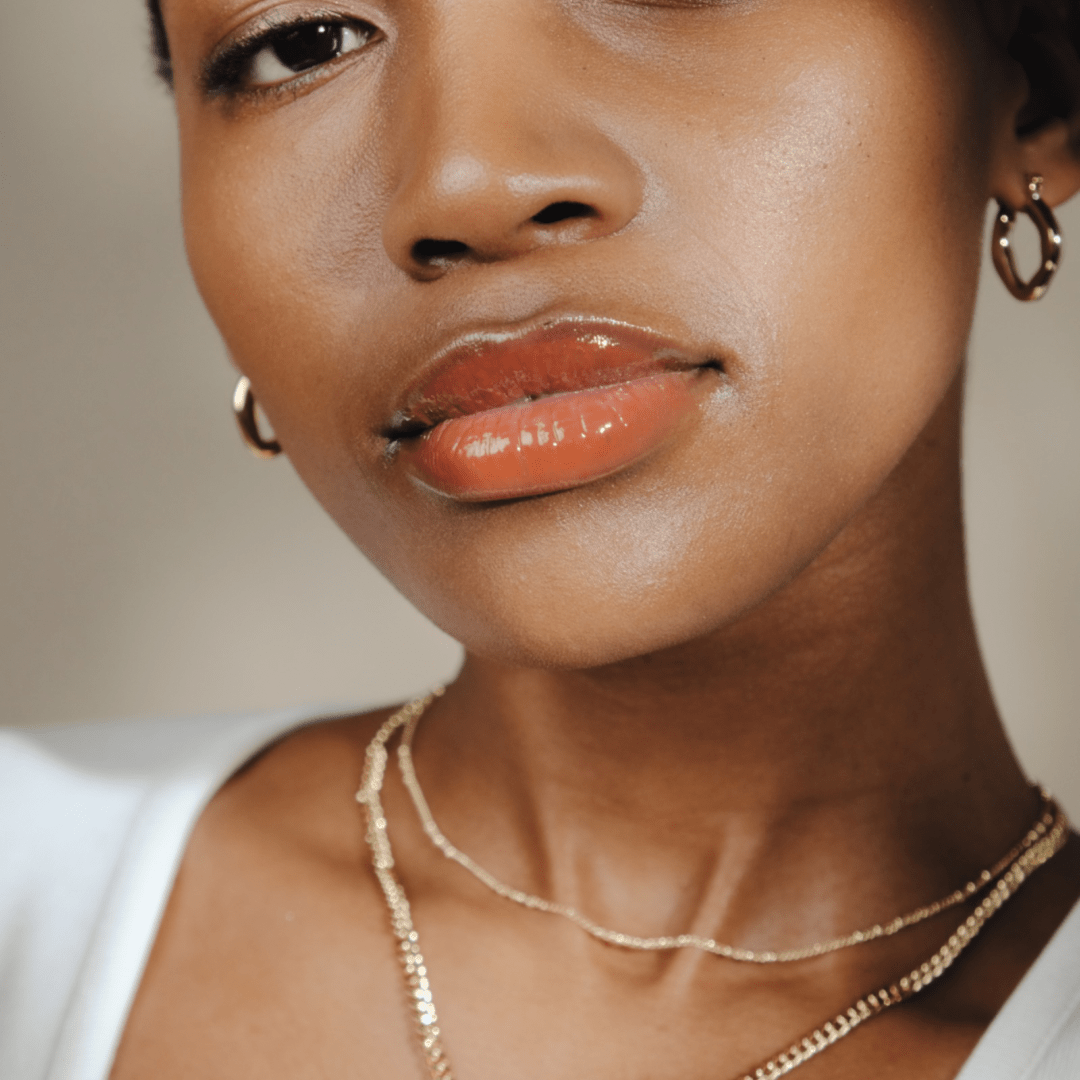 Close-up of a woman's face with glossy lips, gold earrings, layered necklaces, and Chunky Melted Hoop earrings.
