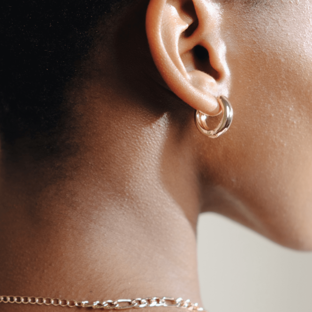 Close-up of a person's ear with a Chunky Huggie Hoop earring and part of a gold necklace.