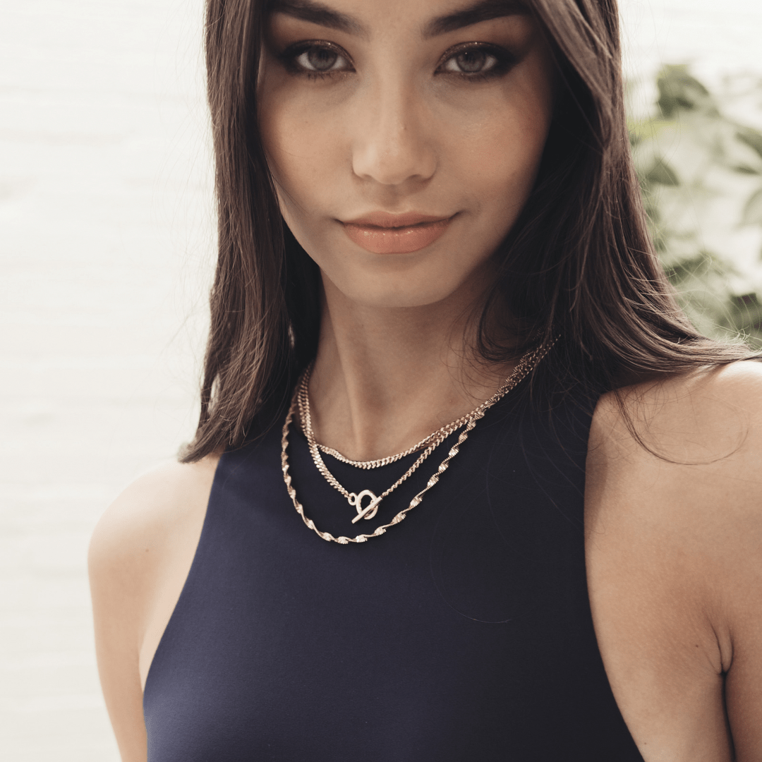 Woman with long brown hair wearing a navy top and layered gold necklaces, featuring an Inter Curb Toggle T-Bar.