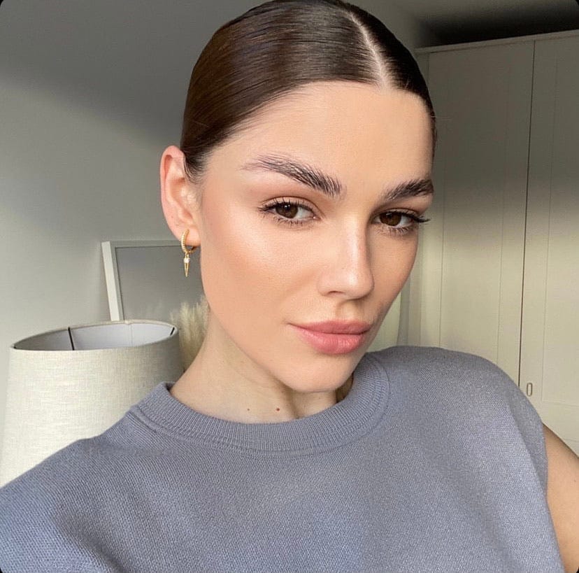Close-up of a woman with brown hair slicked back, wearing a gray sweater and Bar Spear Drop - Silver gold earrings.